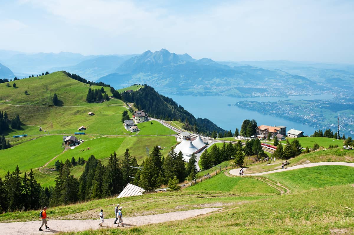 View from Rigi Kulm to Rigi Staffel. The blue trains on the left run on the line from Arth-Goldau, while the red train started in Vitznau. Mount Pilatus and the city of Lucerne can be seen in the background.